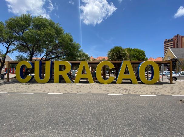 Grote, gele letters vormen het woord "CURACAO" in een buitenomgeving.