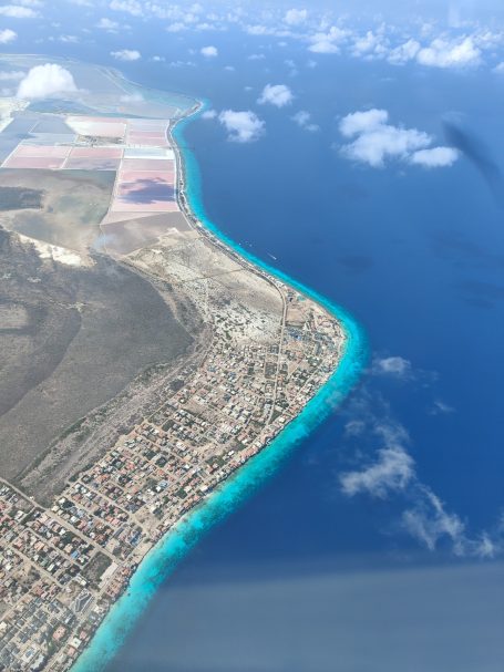 Luchtfoto van een kustlijn met blauwe zee en een stedelijk gebied.