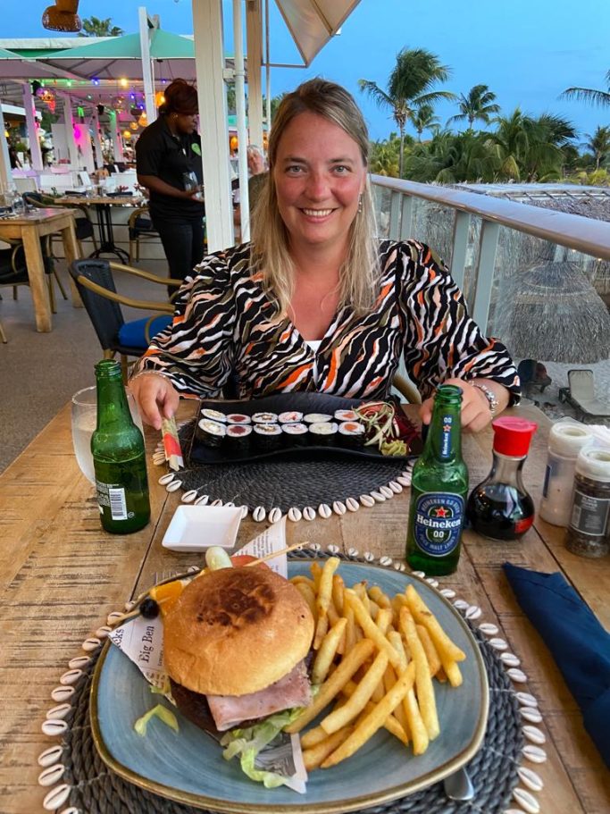 Vrouw met een hamburger en frietjes aan een tafel met uitzicht op zee.