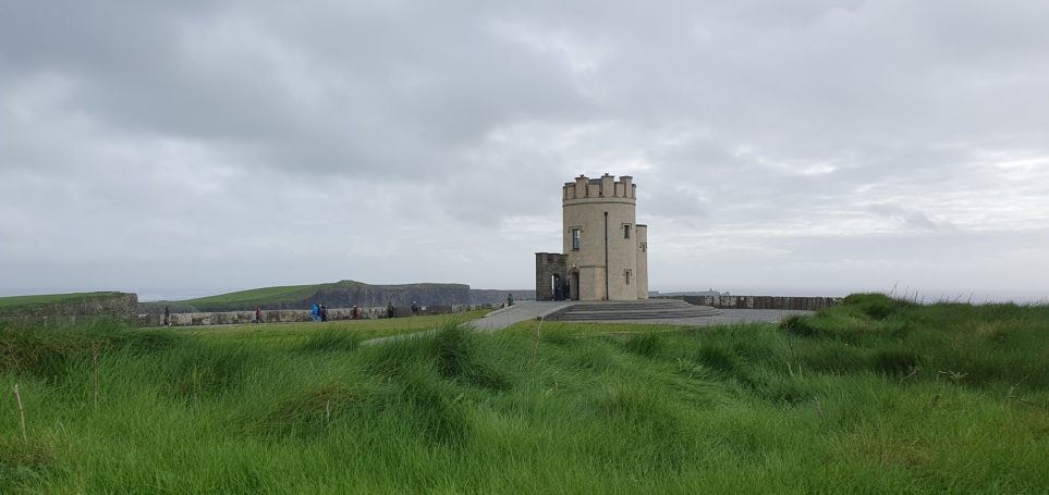 Een oude toren staat op een groene heuvel onder een bewolkte lucht.