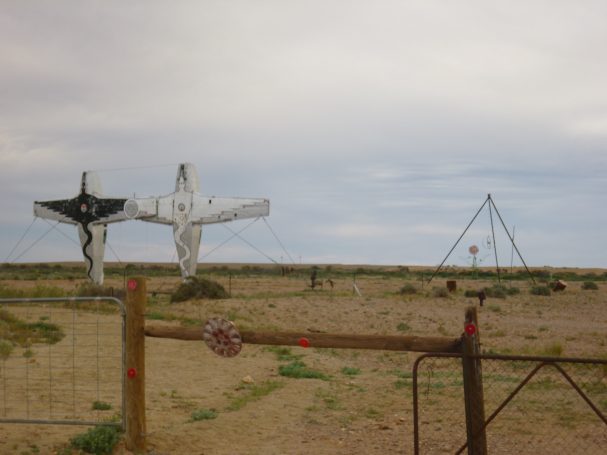 Twee kruisfiguren in een desolate woestijnomgeving met een hek.