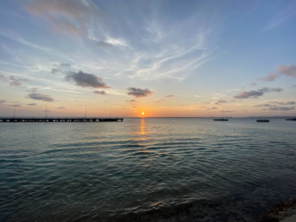 Zonsondergang boven kalm water met wolken en silhouetten van boten in de verte.