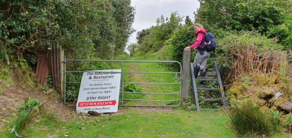 Een vrouw beklimt een ladder om een gesloten hek te passeren op een smal pad.