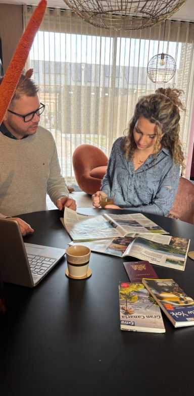 Een man en vrouw bladeren door tijdschriften aan een tafel met een laptop.