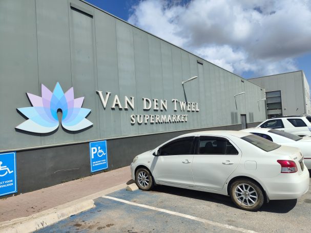 Gebouw van Van den Tweel met een lotuslogo en parkende auto's.