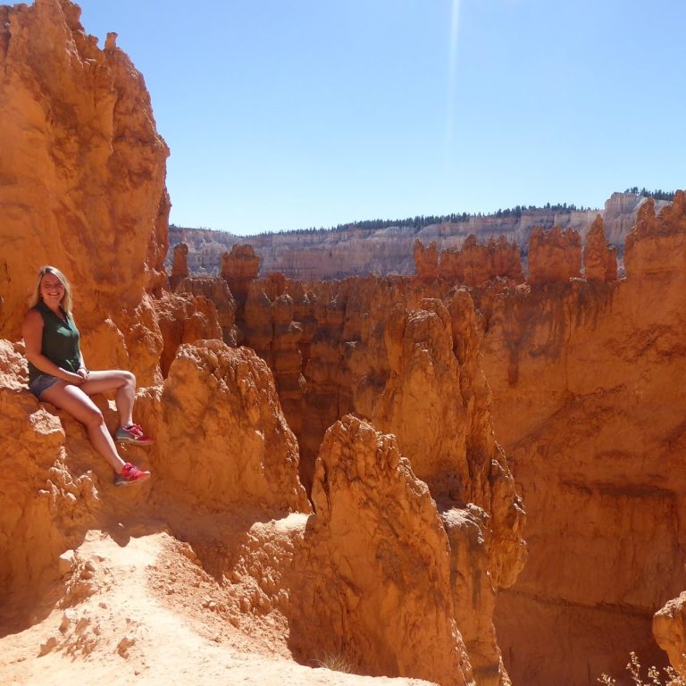 Vrouw zit op een rots in Bryce Canyon, omringd door oranje rotsformaties.