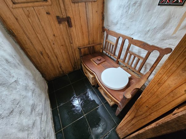 Houten toilet met een rond toiletbril in een rustieke, houten ruimte.