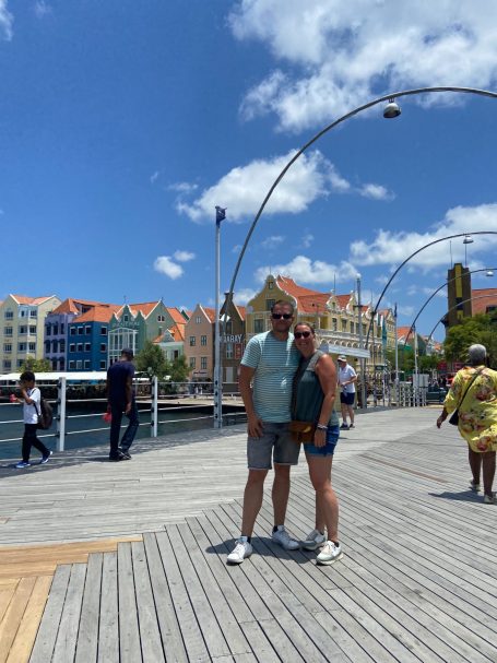 Koppel poseert op gezellige boulevard met kleurrijke gebouwen en blauwe lucht.